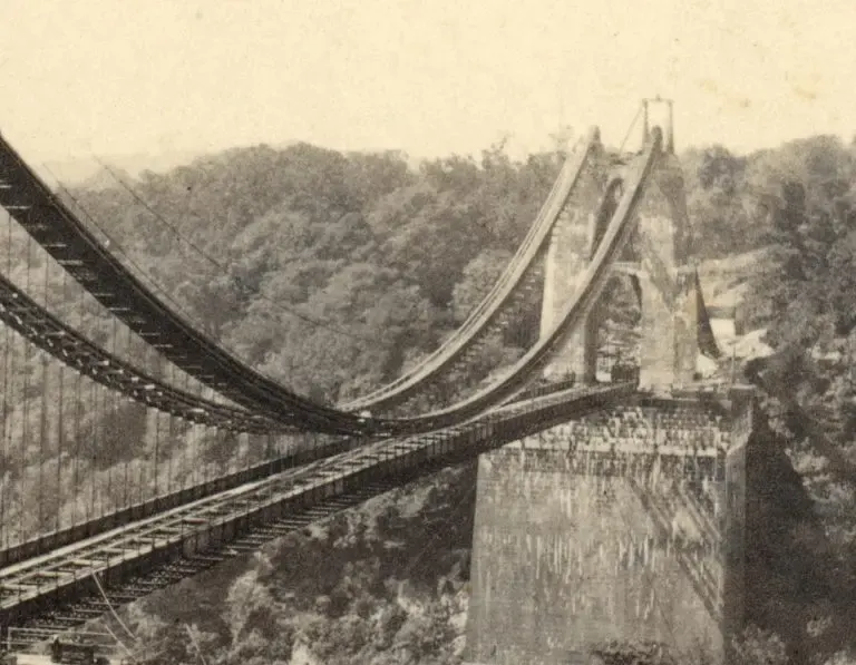 Historic photograph of the Clifton Suspension Bridge's curved track and supporting structures spanning a wooded valley.