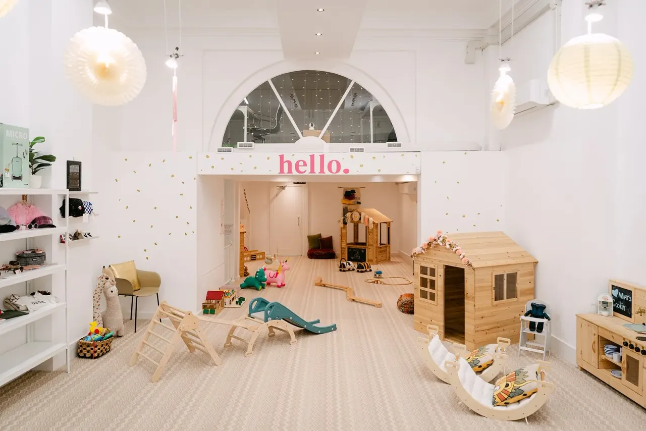 Bright, modern children's play space with wooden play structures, toys, climbing equipment and seating areas beneath decorative pendant lights.