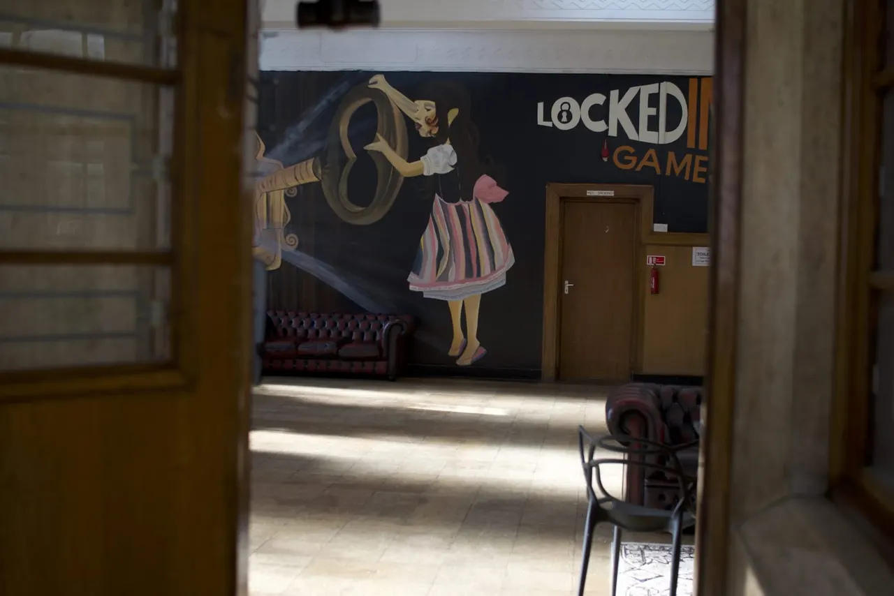 Empty escape game room with a large mural featuring a stylised woman holding a key, and branded signage on the wall.