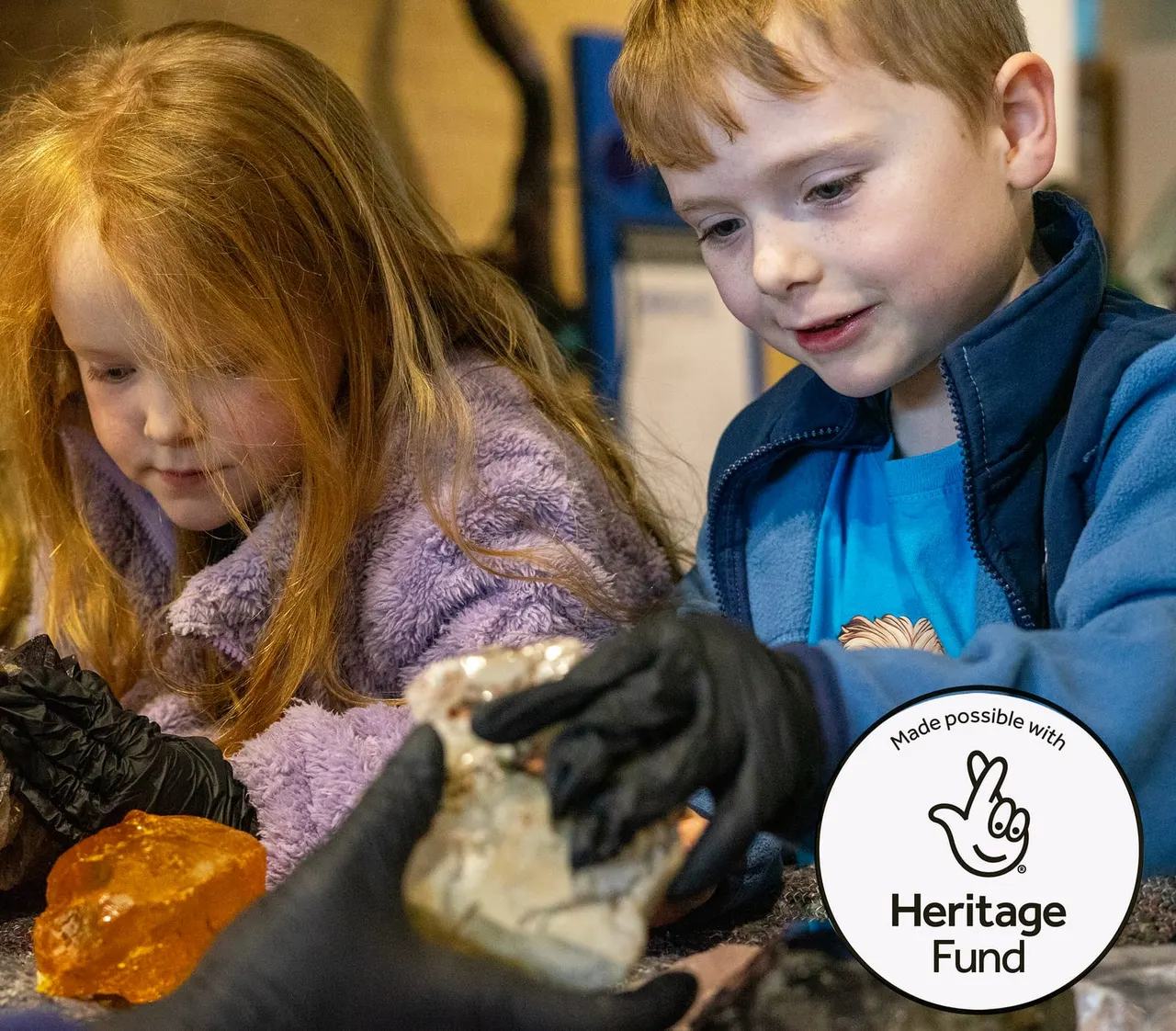 Two young children wearing gloves examine a reptile during a hands-on activity indoors.