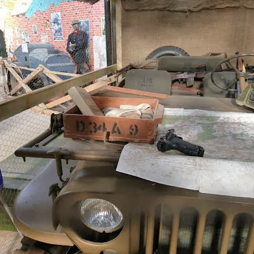 Vintage military vehicles and weapons displayed outdoors at a museum, including a jeep with mounted gun and ammunition boxes.
