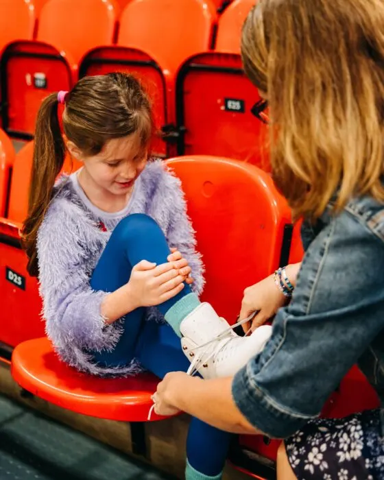 Two young children sitting in bright red stadium seats, one holding a blue cushion.