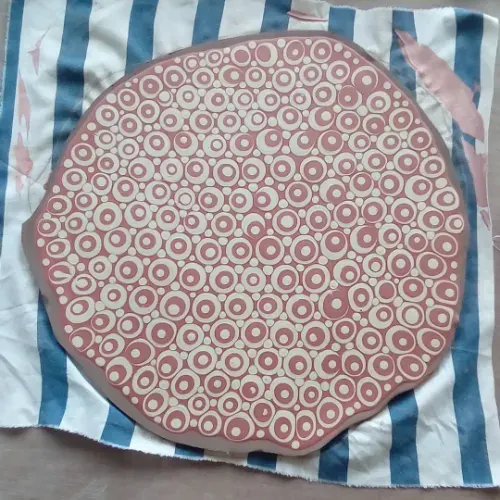 Overhead view of a round ceramic plate with geometric pattern on striped fabric.