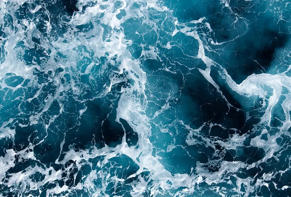 Aerial view of turbulent sea water with white foam and waves from above.