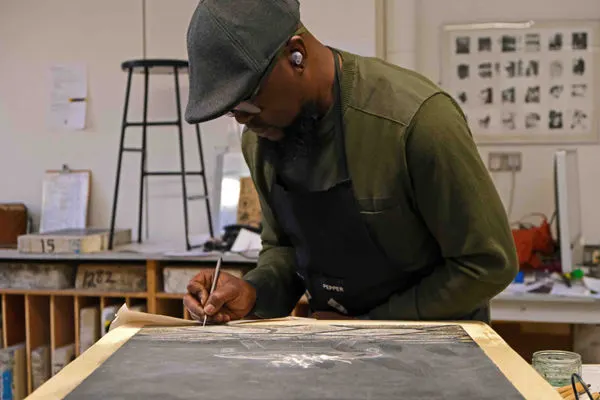 Person in cap and apron working at a printing press in a studio workshop.