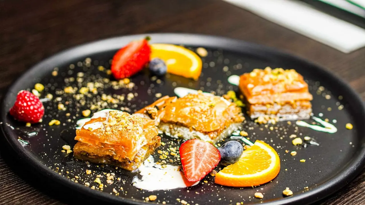 Gourmet dessert plate with layered pastry, berries, citrus slices and gold leaf garnish on black plate.