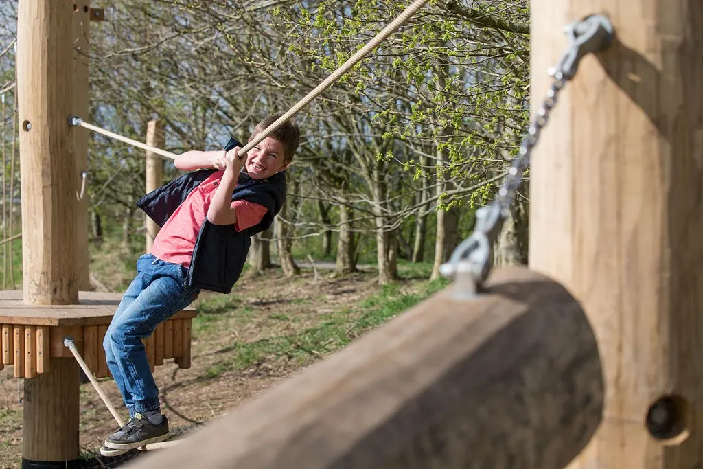 Child swinging on a rope across a woodland adventure course.