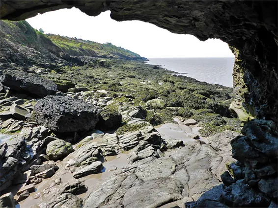 View from inside a sea cave looking out to a rocky coastline with moss-covered stones and sea beyond.