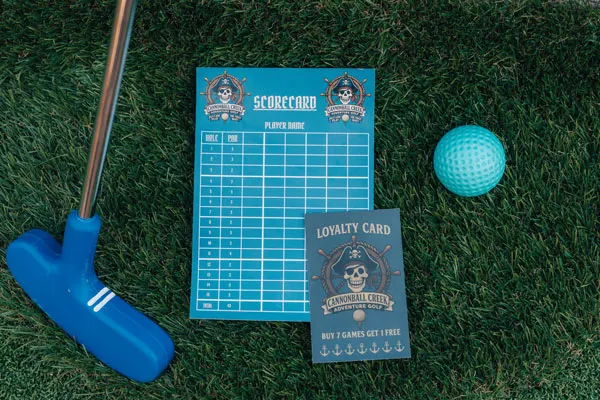 A blue putter, turquoise golf ball, scorecard and loyalty card arranged on artificial grass.