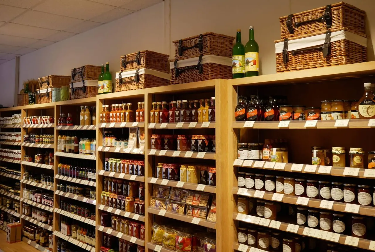 Shelves stocked with bottled beers, jars of preserves, condiments and wicker baskets in a farm shop.