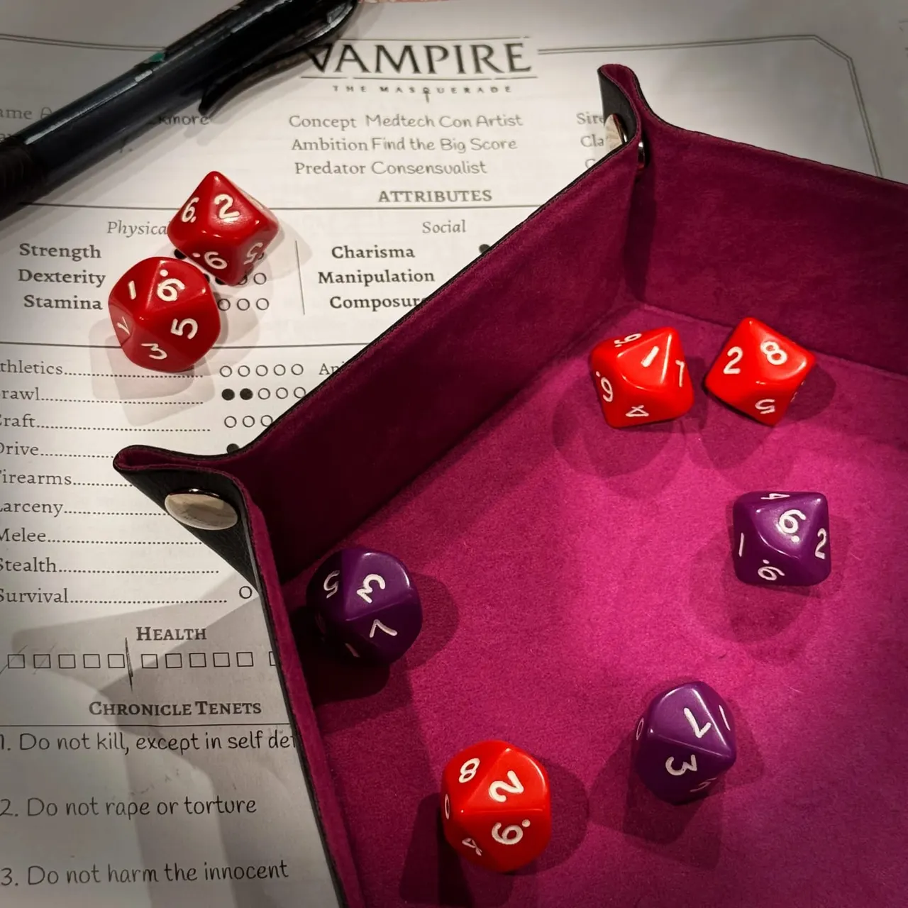 Vampire: The Masquerade character sheet with polyhedral dice in a burgundy dice tray and rulebook.