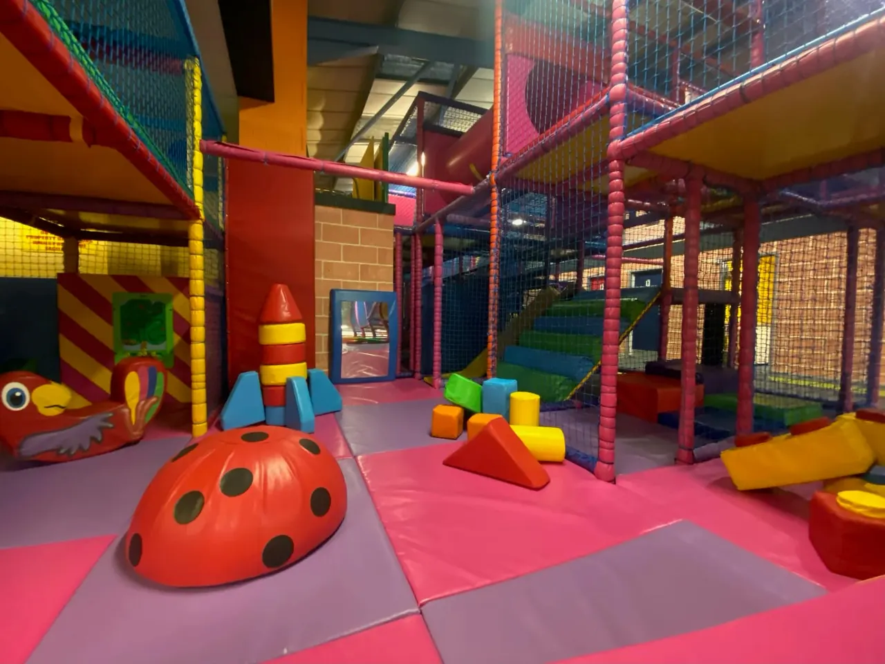Colourful indoor play area with foam climbing structures, a red ladybird dome, building blocks and netting, designed for young children.