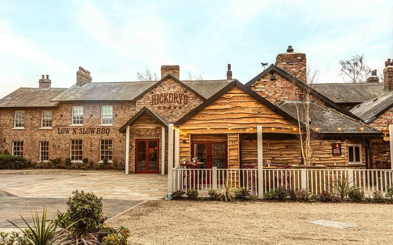 A brick smokehouse and low 'n' slow BBQ restaurant with wooden frontage, red doors, and a covered porch with white railings, set around a courtyard.