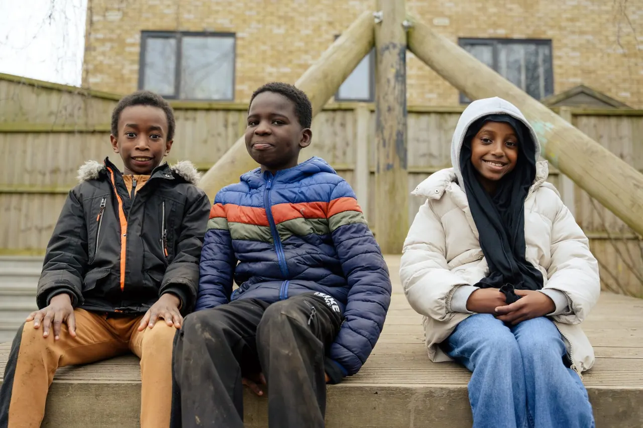 Three young people sitting together on wooden steps at an outdoor leisure facility.