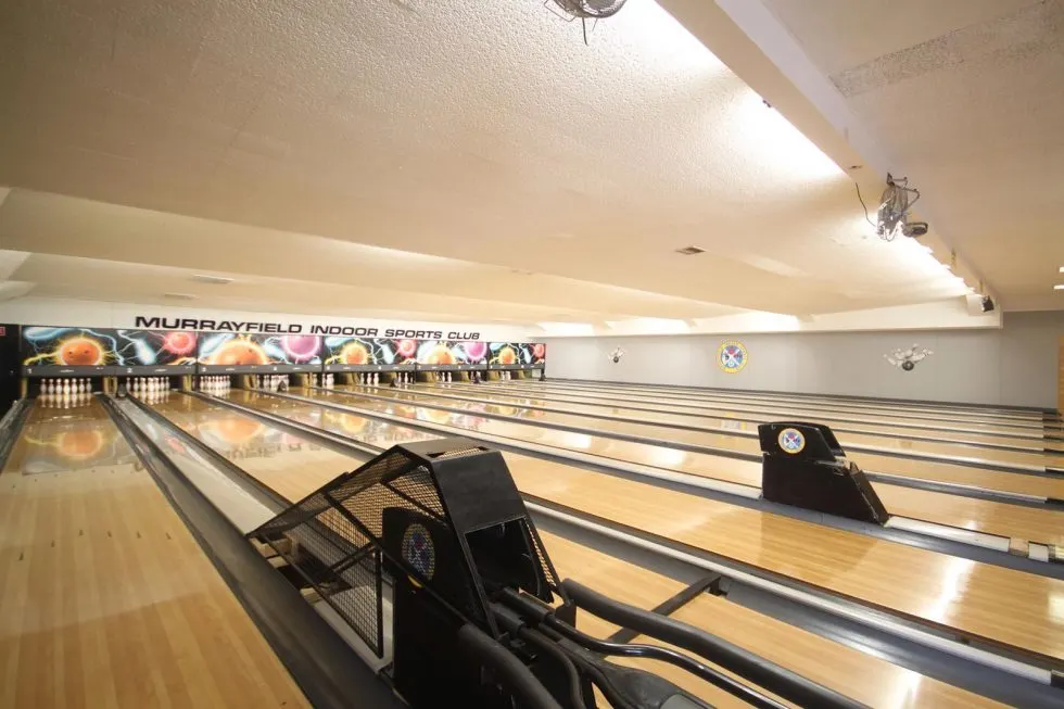 Multiple bowling lanes with polished wooden surfaces and automated scoring equipment at an indoor bowling alley.