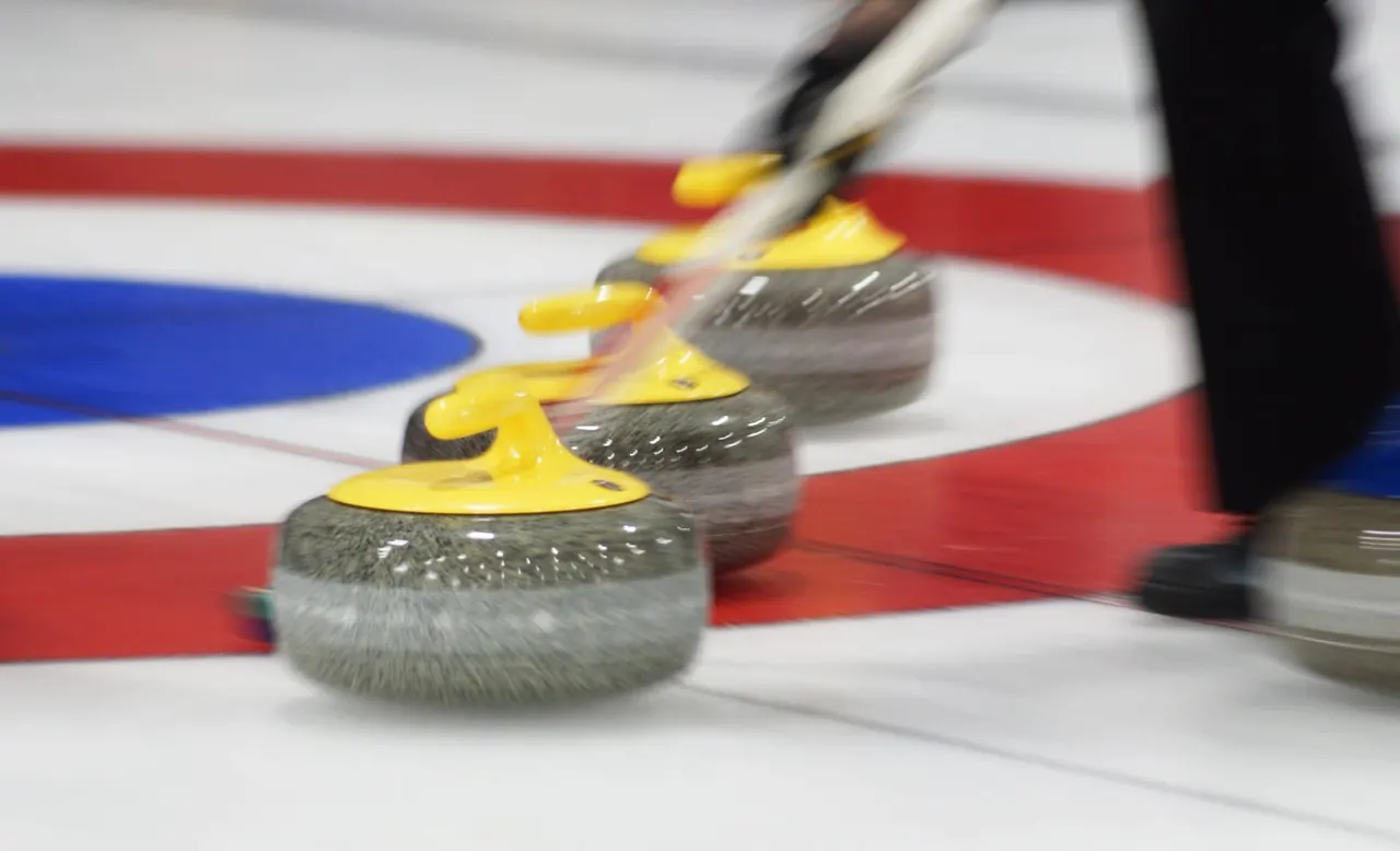 Curling stones with yellow handles lined up on an ice rink with red and blue target markings.
