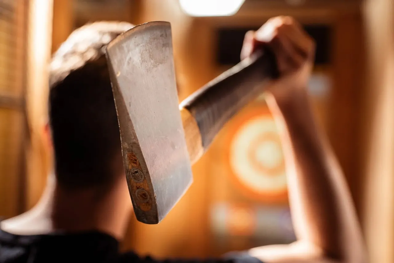 Close-up of a person's hand holding an axe, ready to throw in an indoor wooden facility.