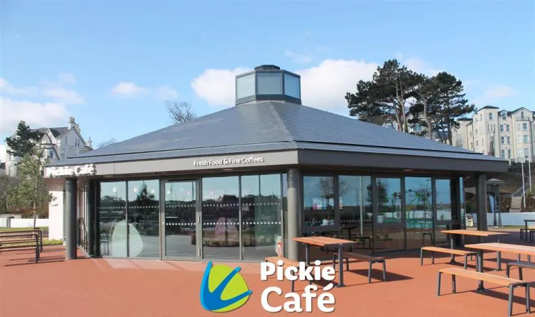 Modern circular café building with large windows and outdoor seating area on red tarmac.