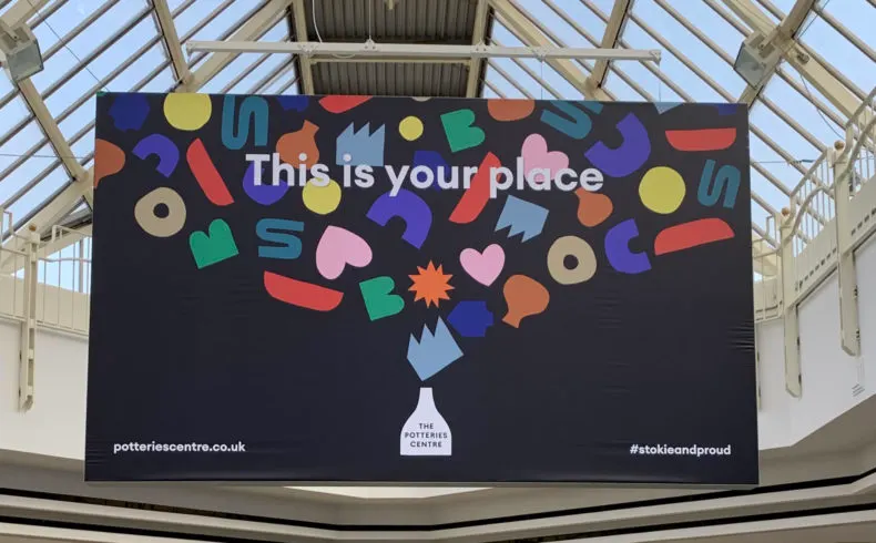 A large promotional banner hangs from a glass-roofed ceiling, displaying colourful abstract shapes and the text "This is your place".