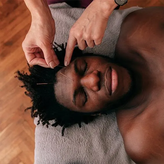 Man receiving a facial massage or spa treatment while lying on a padded surface.