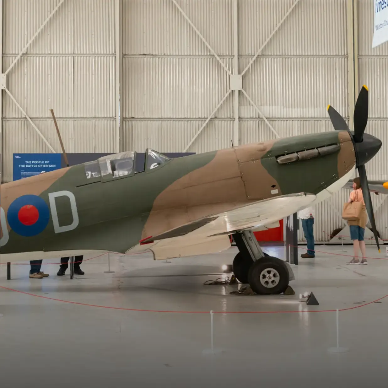 Visitors view a vintage Second World War fighter aircraft displayed indoors in a hangar.