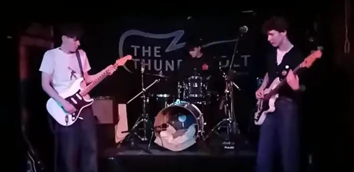 A rock band performs on stage with two guitarists and a drummer during a live concert.