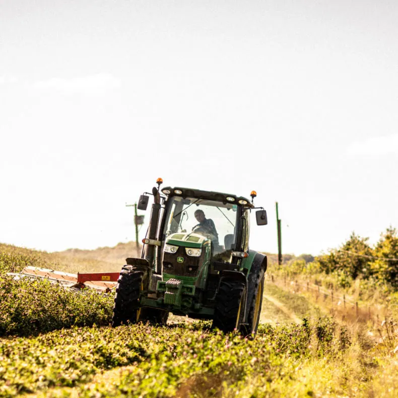 Green tractor with operator harvesting crops in a sunny field.