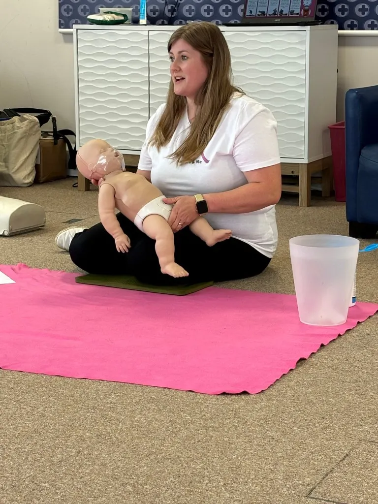 Instructor demonstrating infant care techniques with a practice baby doll during a parent-baby class.