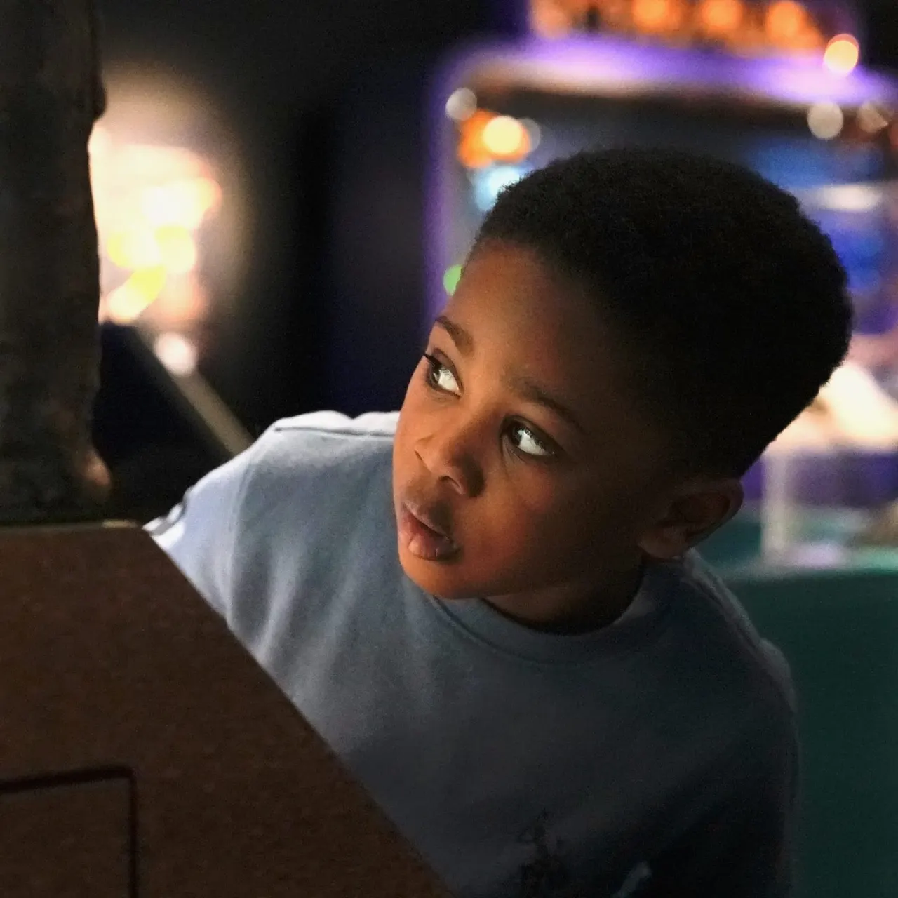Child looking at an illuminated display at night with coloured lights in the background.