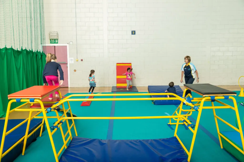 Children playing on trampolines and climbing equipment in an indoor sports hall.
