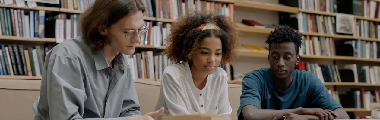 Three people sitting at a table in a library with bookshelves behind them.