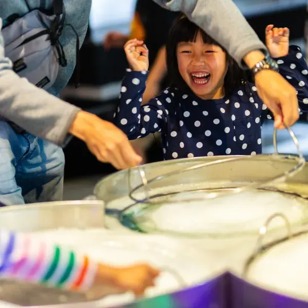 Young child laughing with hands on head while interacting with a large fish in a touch tank.