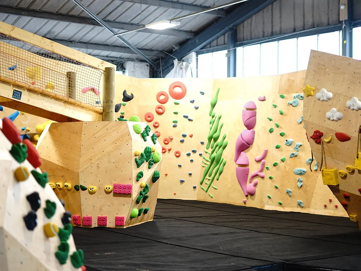 Multiple wooden climbing walls with coloured holds inside an indoor leisure facility.