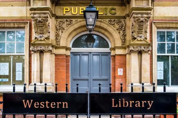 Historic stone public library building entrance with blue double doors, ornate carved capitals, and black metal railings.