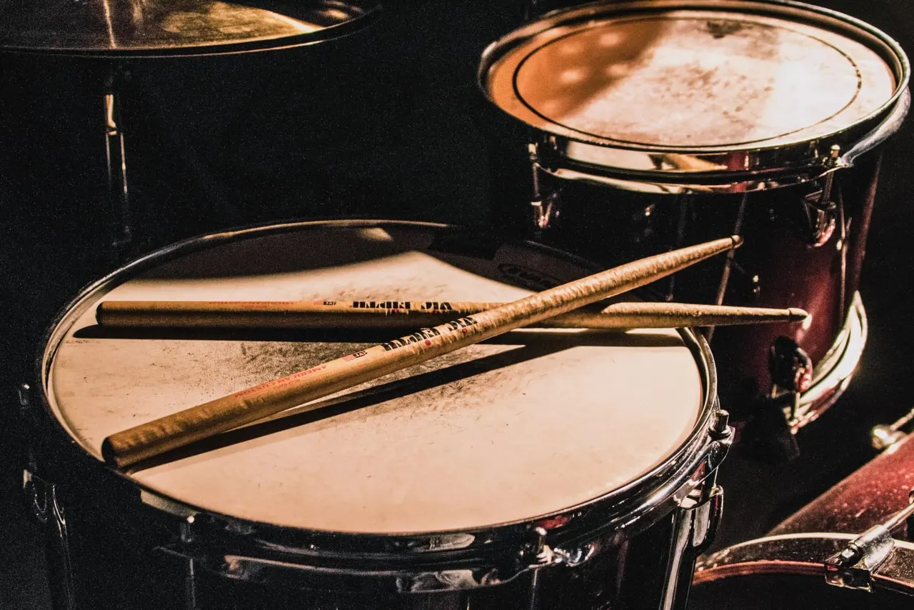 Drum kit with drumsticks resting on white drum heads against a dark background.