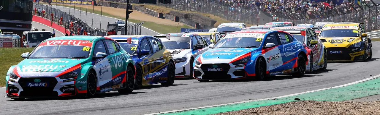 Multiple racing cars competing in a touring car race on a circuit track with spectators in grandstands.