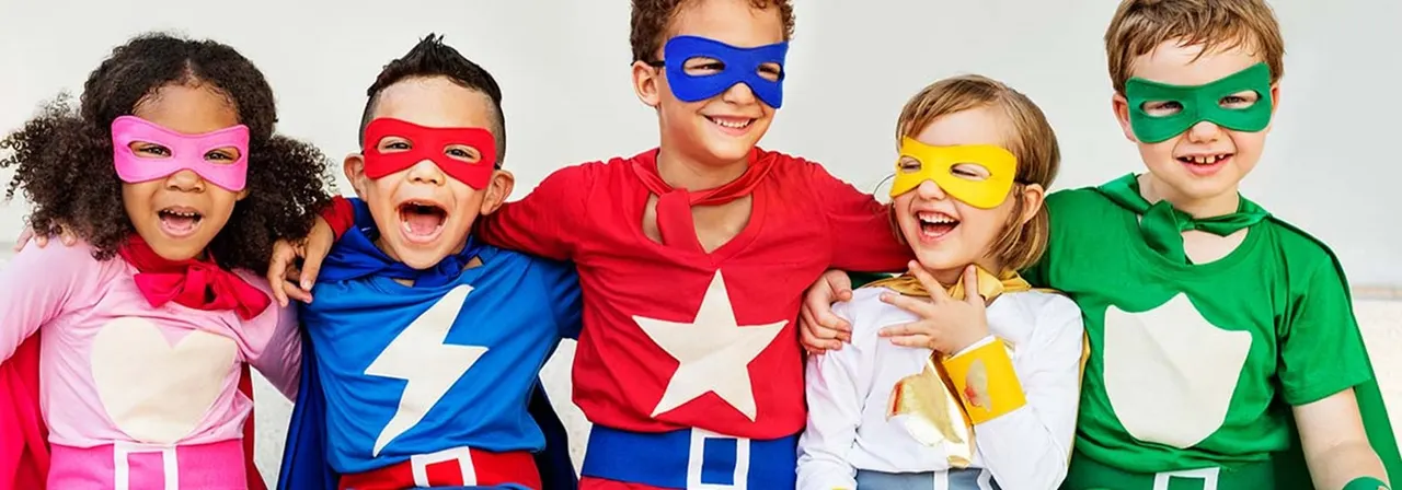Five children wearing coloured superhero masks and capes smile at the camera.