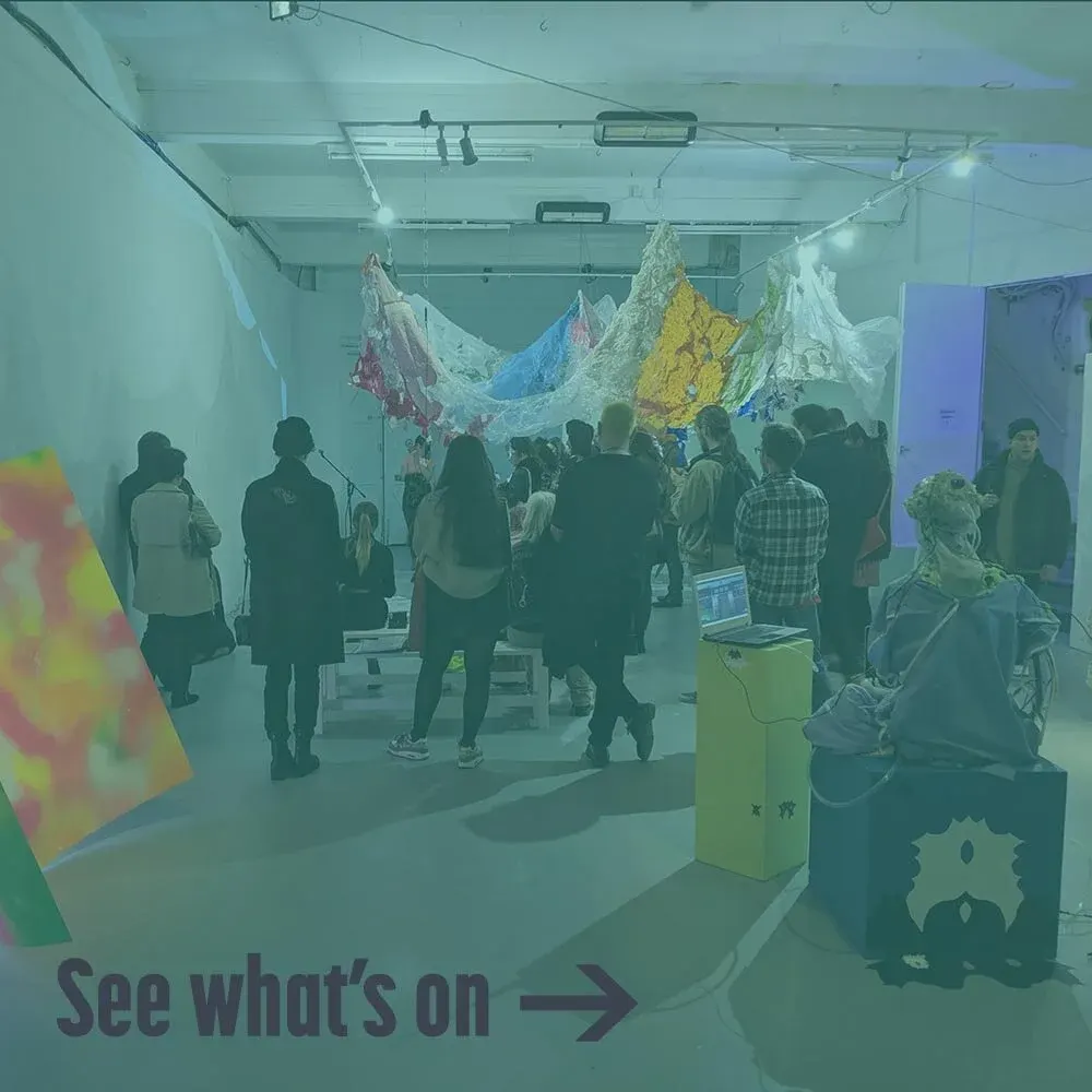 Visitors exploring an art gallery exhibition with colourful fabric installations and mountain-like sculptures suspended from the ceiling.