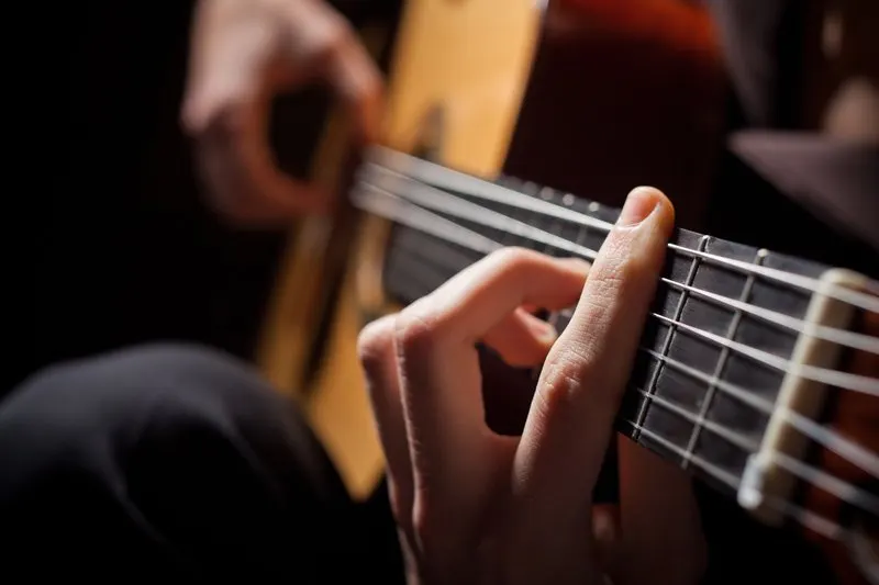 Musician's hand on the fretboard of an acoustic guitar during a performance.