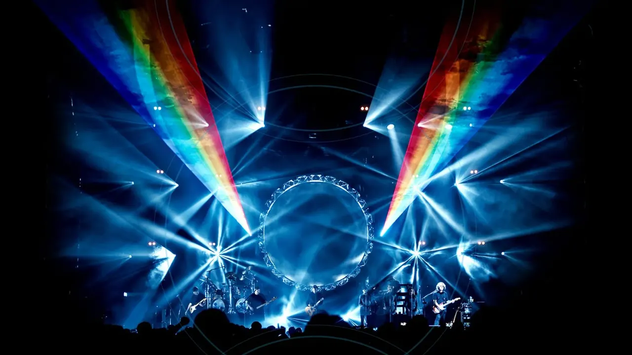 Live band performing on stage with spectacular laser light show featuring blue and rainbow-coloured beams radiating across the venue with audience silhouettes in foreground.
