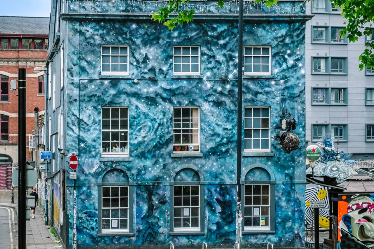 Large building facade covered in blue and teal mural artwork depicting a starry night sky and clouds.