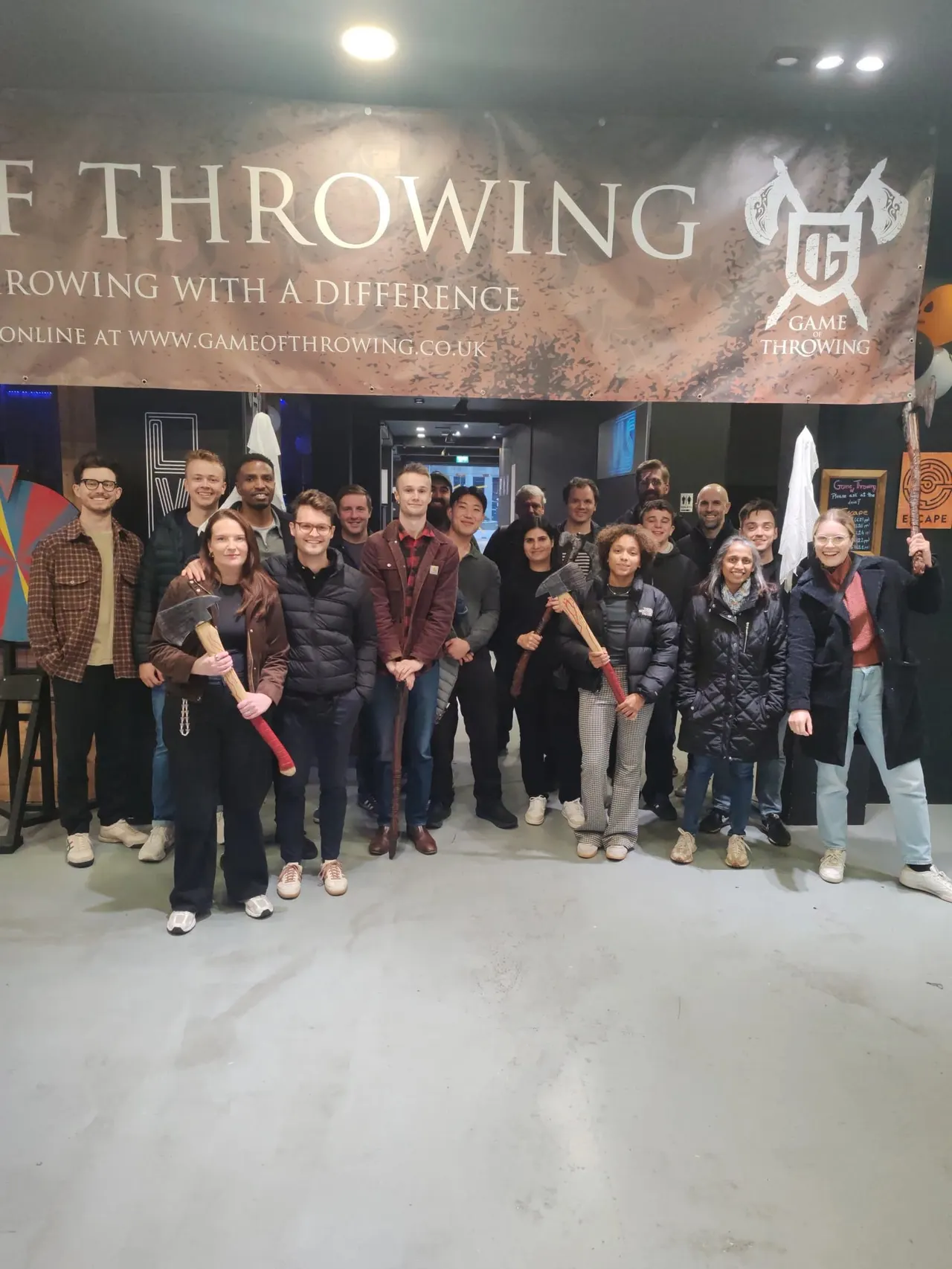 Large group of people holding axes posing for a photo at an indoor axe-throwing venue.