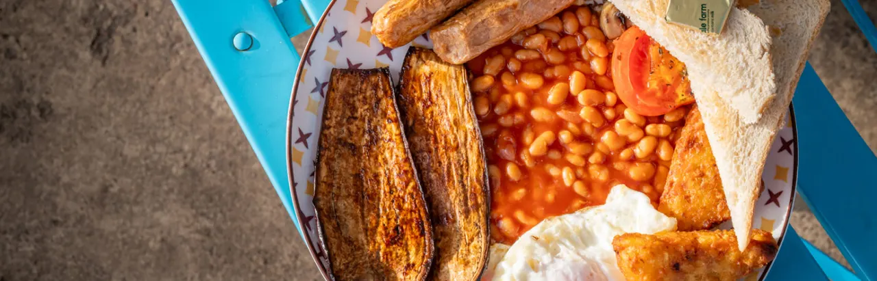 Plate of cooked sausages, baked beans, fried bread and tomato slice on decorative tableware.