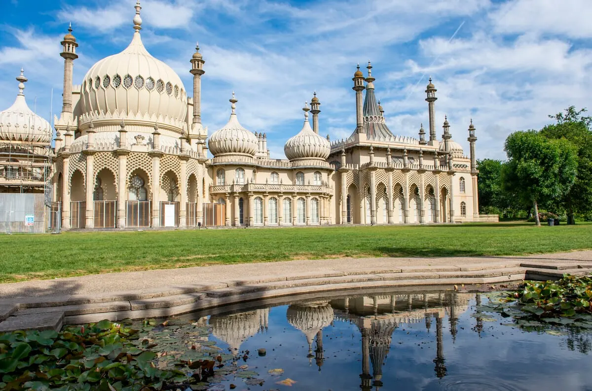 Ornate cream-coloured domed building with minarets reflected in a pond under blue sky.
