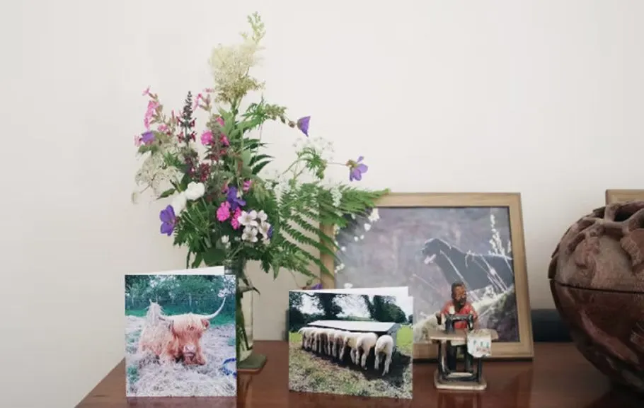 A display shelf with framed farm photographs, a vase of mixed flowers in pink and purple tones, and decorative items.