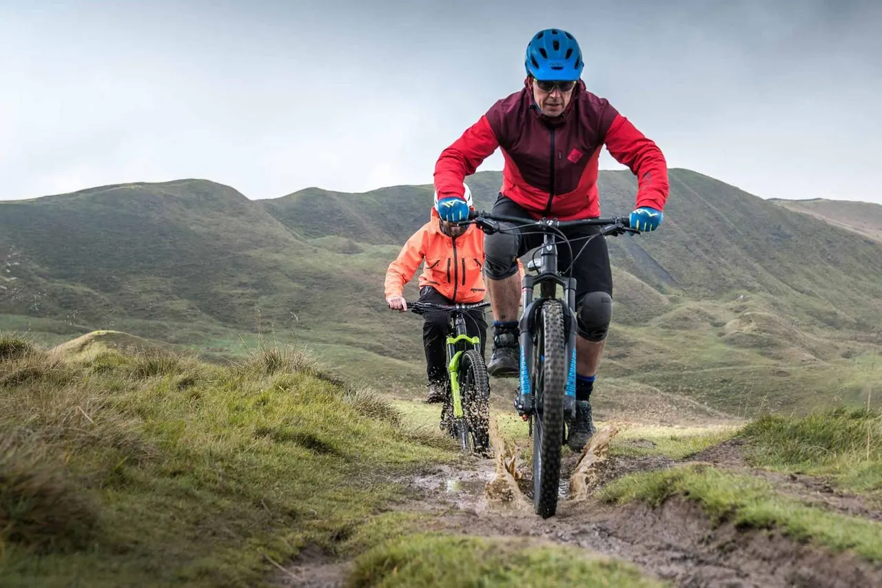 An adult and child mountain biking on a trail through rolling moorland hills.