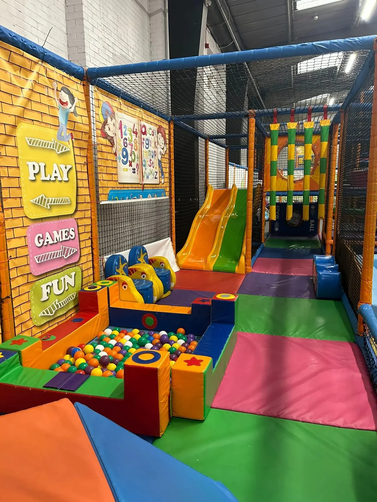 Indoor play area with colourful foam mats, slides, ball pit, climbing structures and game signage for children's entertainment.