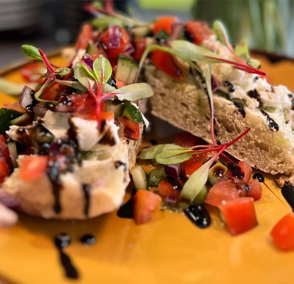 Gourmet open sandwiches topped with fresh vegetables, microgreens and sauce on a yellow plate.