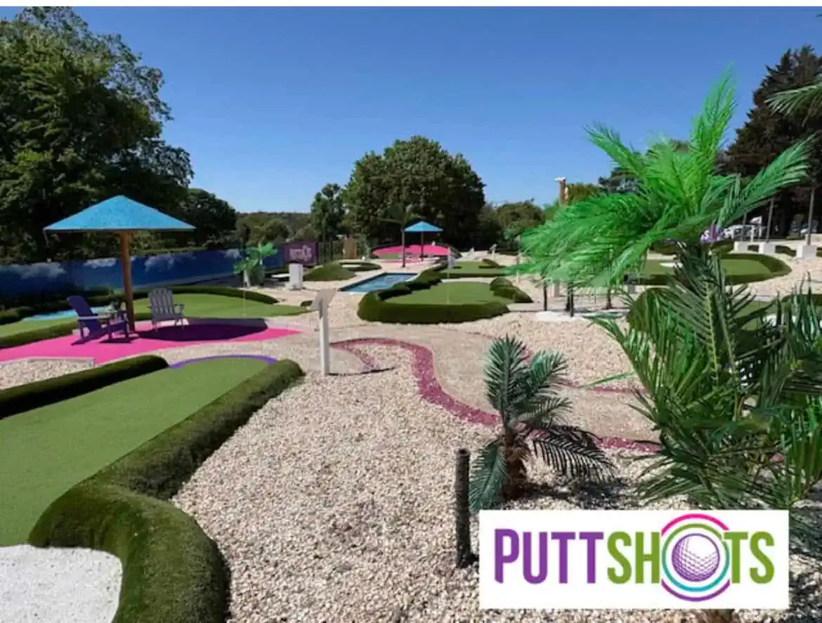 Colorful mini golf course with multiple holes, palm trees, manicured hedges and umbrellas on a sunny day.