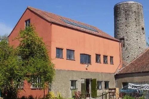 Stone tower and terracotta-painted historic building with solar panels under clear blue sky.